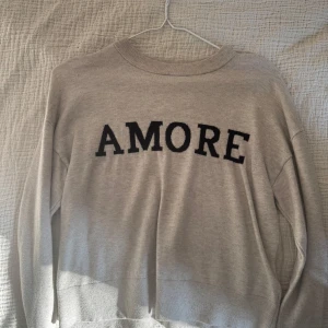 Söt stickad tröja - Jättefin beige stickad långärmad tröja från Gina young med svart texten 'AMORE' framtill. Tröjan är i mjukt material och är knappt använd (Inga defekter). Pris kan diskuteras!