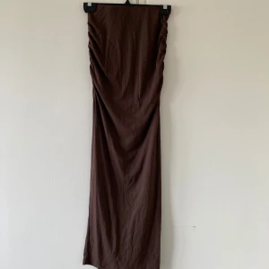 Brun långkjol från Gina Tricot - Säljer en brun långkjol från Gina Tricot i mjukt material. Kjolen har en tight passform och rynkade detaljer längs sidorna upptill. Perfekt för dig som gillar minimalistisk stil och vill ha en enkel men snygg kjol.