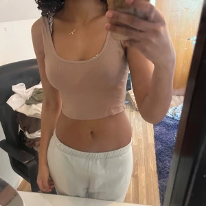 Beige croppad ribbad linnetopp - Säljer en beige croppad linnetopp med ribbad struktur. Toppen har breda axelband och rundad halsringning. Perfekt för varma dagar eller som lager under en skjorta.