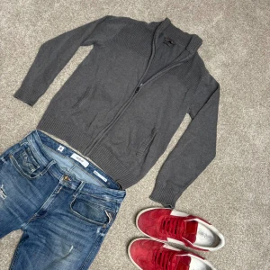 Grå stickad kofta med dragkedja - Storlek M, köp för endast 199. En stilren grå stickad kofta med dragkedja framtill och ribbade muddar vid ärmslut och nederkant. 