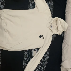 Vit hoodie från Off-White - Vit hoodie från Off-White med svart logga på bröstet och stort grafiskt tryck med pilar på ryggen. Klassisk känguruficka framtill och huva. Perfekt för en stilren streetwear-look.