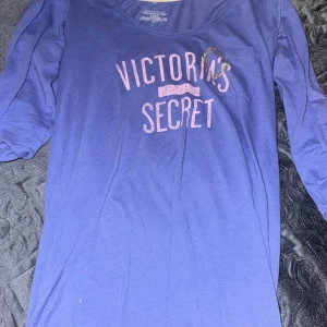 Nattlinne - Lila långärmad tröja från Victoria's Secret med tryckt logga i rosa och glitter på bröstet. Tröjan har rund halsringning och knappar på ärmarna för att kunna vika upp dem. Perfekt för en avslappnad stil. Använd 1-2 gånger. Mycket bra skick!!