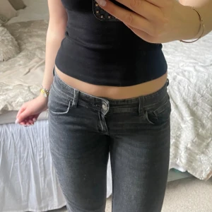 Svarta bootcut jeans med fickdetaljer - Säljer ett par svarta bootcut jeans med snygga fickor bak och silverfärgade knappar. Jeansen har låg midja och klassisk femficksdesign. Perfekta till en enkel topp eller hoodie.