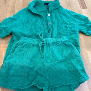 Turkosa shorts med knytband & skjorta - Säljer ett par turkosa shorts och skjorta från Shein i mjukt, krinklat bomullstyg. Shortsen har resår i midjan och knytband framtill för extra komfort. Perfekta för varma dagar och har en avslappnad passform.