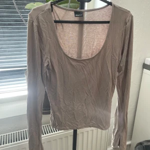 Beige långärmad topp från Gina Tricot - Säljer en beige långärmad topp från Gina Tricot med rund, djup ringning. Toppen är i ett tunt och lätt material och har en liten slits i sidan av ärmen. Perfekt för lager-på-lager eller som basplagg.