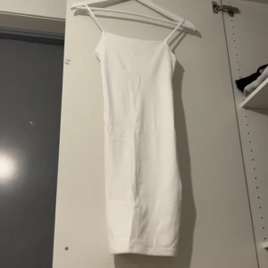 Vit tight axelbandslös klänning - Säljer en stilren vit klänning med smala axelband och tight passform. Klänningen är enkel och rak i modellen, perfekt för dig som gillar minimalistisk stil. Längden är mellan knä och vad.