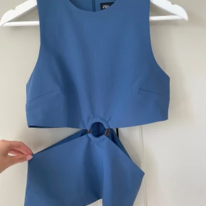 Blå topp från ZARA - Trendig blå croppad linnetopp från ZARA med rund halsringning och snygg detalj med ring på framsidan. Perfekt för att skapa en cool och modern look.