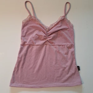 Ljusrosa topp med spets och pärlor - Supersöt ljusrosa linnetopp med tunna axelband, spetsdetaljer och små pärlor längs urringningen. Toppen har rynk framtill och är perfekt för en somrig look.