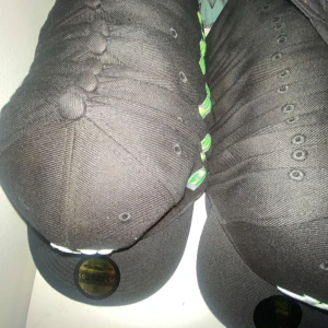 Svart och grå keps med regnbågsfärgade detaljer och loggor - Säljer flera kepsar från New Era, bland annat med New York Yankees och Chicago Bulls logga. Vissa kepsar har regnbågsfärgade stänk och andra har klassisk svart design. En keps har röd skärm och Chicago Bulls broderad framtill.