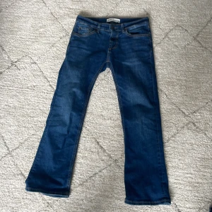 Blå bootcut jeans - Snygga blå jeans med bootcut passform och klassisk femficksdesign. Jeansen har lowwaist midja och är tillverkade i ett stretchigt denimtyg som ger en bekväm känsla. Perfekta för dig som gillar en tidlös stil med lite utsvängda ben.
