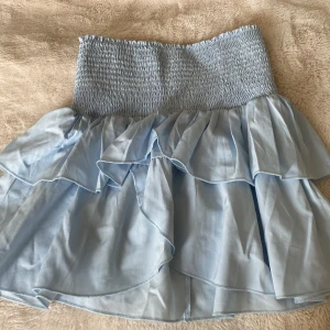 Ljusblå volangkjol från Neor Noir - Supersöt ljusblå kjol från Neor Noir med smockad midja och dubbla volanglager. Kjolen har en luftig och flowy känsla, perfekt för varma dagar. Den är köpt från Nelly och nästan helt oanvänd, köpt för 499kr💗. 