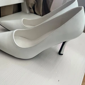 Vita pumps med spetsig tå från Boohoo - Säljer ett par klassiska vita pumps från Boohoo med spetsig tå och smal klack. Skorna har en stilren design och är tillverkade i syntetmaterial. Perfekta för dig som vill ha en elegant look.