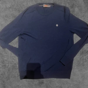 Mörkblå tröja från Morris - Säljer en stilren mörkblå tröja från Morris i storlek S. Tröjan är tillverkad i merinoull och har en liten broderad logotyp på bröstet. Perfekt för en klassisk och bekväm look. Säljer denna då jag vill hitta något nytt! Kostar 1400kr ny i butik. Tröjan har krympt lite grann sitter mer som en xs  