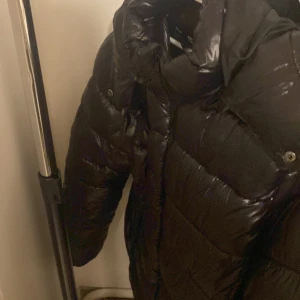 Svart pufferjacka med huva - Säljer en svart pufferjacka från 157 i storlek L. Jackan har glansigt material, huva och två stora dragkedjefickor framtill. Perfekt för kyliga dagar och enkel att matcha med olika outfits.