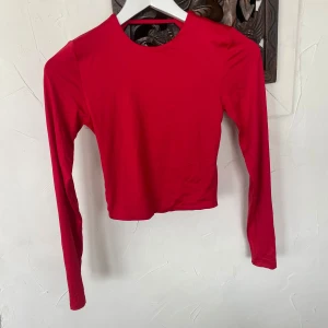 Röd långärmad topp med öppen rygg från New Yorker - Säljer en röd långärmad topp från New Yorker i storlek XS. Toppen har en croppad passform och en snygg öppen rygg med twistad detalj. Perfekt för dig som vill sticka ut med en enkel men cool look.