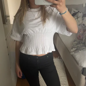 Vit croppad plisserad topp - Säljer en vit croppad topp med plisserad midja och korta ärmar. Toppen har en lätt volang nertill och är i ett mjukt material som ger en snygg siluett. Perfekt att styla med både jeans och kjol. Den är använd en gång så den är i nyskick, den är i storlek M men skulle säga att den är som en S💓