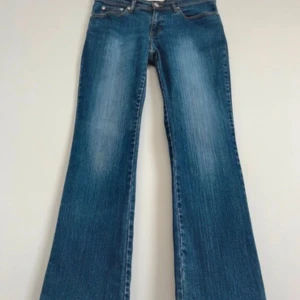 Blå bootcut jeans med detaljer - Säljer ett par blå bootcut jeans med låg midja och klassisk femficksdesign. Perfekta för dig som gillar en vintage look. Midjemått: 40 hm tvärsöver. Innerbenslängd: 80 cm. Total längd: 104 cm. 