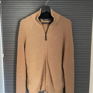 J.Lindeberg Fullzip Kofta - Säljer en beige stickad kofta från J.Lindeberg. Tröjan är i mycket bra skick, kan vara lite nopprig på vissa ställen. Tröjan är stl M men passar även fint på de som bär stl L.