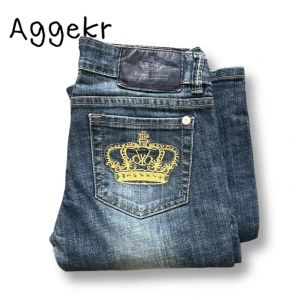 Bootcut Victoria Beckham Jeans - Snygga blå jeans med slitningar och unika gula kronbroderier på bakfickorna. Jeansen har klassisk femficksdesign och lätt utsvängda ben. Perfekta för dig som vill sticka ut med detaljer.