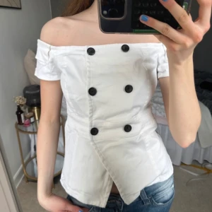 Vit offshoulder blus med knappar - Snygg vit offshoulder blus med svarta knappar framtill. I demin material
