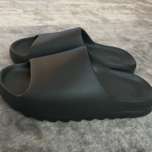 Gråa slides från Adidas - Säljer ett par gråa slides från Adidas knappt använda. Tillverkade i syntetmaterial med räfflad sula för extra grepp. Perfekta för sommaren eller att ha på stranden.  Storlek us 48.5