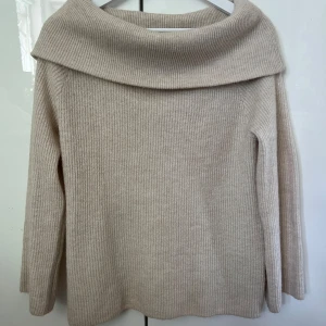 Beige ribbad stickad tröja H&M - Supermysig beige stickad tröja från H&M med bred, vikt krage som ger en chill och snygg look. Tröjan är ribbstickad och har långa ärmar, perfekt för lager på lager under höst och vinter. Enkel att matcha med jeans eller kjol.