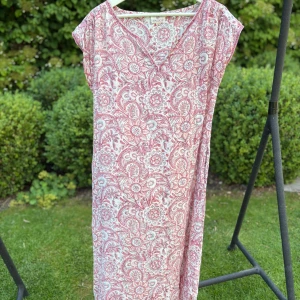 Blommig sommarklänning från Anokhi - Luftig och skön klänning från Anokhi i vitt och rosa med blommigt mönster. Modellen är rak med v-ringning och korta ärmar, perfekt för varma dagar. Tillverkad i mjuk bomull som känns lätt mot huden.