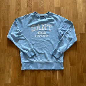 Ljusblå vintage sweatshirt från GANT - Snygg ljusblå sweatshirt från GANT med tryck 'GANT 1949 NEW HAVEN' på bröstet. Tröjan har rund hals, långa ärmar och ribbade muddar. Perfekt för en chill och sportig look. Tillverkad i mjuk bomull för extra komfort. Använt några gånger men inte några tecken på användning som märks👍 Kom gärna med offer eller frågor🙌