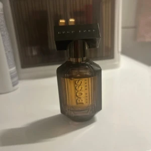 Hugo  BOSS parfym  -  parfym från Hugo Boss i en stilren, mörkbrun glasflaska med guldiga detaljer, Flaskan har en robust, kantig form och BOSS-loggan syns tydligt på framsidan. Perfekt för dig som gillar exklusiva dofter.