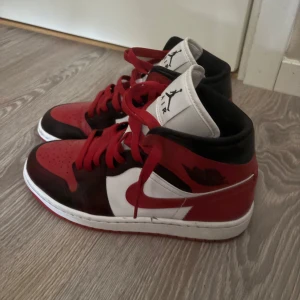 Nike Air Jordan 1 Mid röd/svart/vit - Säljer ett par Nike Air Jordan 1 Mid i klassiska färger: rött, svart och vitt. Skorna har röd sula, röda snören. Använd 1-2 gånger 