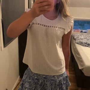 Vit blus med volang - Söt vit blus med broderade hål och spetsdetalj över bröstet. 