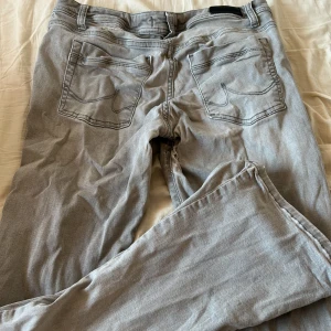 Ljusgrå jeansbyxor med raka ben - Säljer ett par ljusgrå jeansbyxor med klassisk femficksdesign och raka ben. Byxorna har bälteshällor och synliga sömmar. Perfekta för dig som gillar en enkel och clean look. Materialet är mjukt och skönt bomullsjeans.