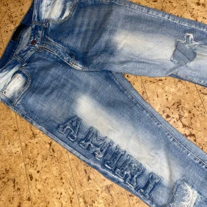  jeans från Amiri - Säljer ett par blå  jeans från Amiri med slitna detaljer och tydlig logotyp i denim på vänster ben. Jeansen har en tvättad look, klassiska fem fickor och dragkedjegylf. Perfekta för dig som gillar streetstyle och vill sticka ut.
