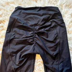 Svarta shorts från ICANIWILL XS - Svarta shorts från ICANIWILL i storlek XS. De har hög midja, scrunch-detalj bak och är tillverkade i ett stretchigt material som passar perfekt för träning. Snygg logga framtill och figurnära passform.