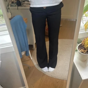 Svarta kostymbyxor från Lindex - Snygga kostymbyxor från Lindex, modell Fiona, i bootcut-modell med hög midja. Byxorna har klassisk dragkedja och knapp framtill. Perfekta till en clean och stilren look. Materialet känns mjukt och följsamt.