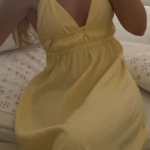 Gul sommarklänning med v-ringning - Söt gul klänning med djup v-ringning och smala axelband. Klänningen har en markerad midja och ett luftigt, flowy tyg som passar perfekt för varma dagar. Enkel och stilren design som ger en fräsch look.