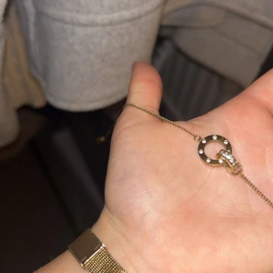 Guldigt halsband med cirkel och stenar - Snyggt halsband i guld med en tunn kedja och ett cirkelformat hänge dekorerat med små glittrande stenar. Perfekt för att ge din outfit lite extra bling och stil.