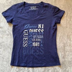 Mörkblå t-shirt från Guess med tryck v ringad - Supersnygg mörkblå tshirt från Guess med tryck. V-ringad, bra skick, inga defekter. Står ingen storlek men skulle säga S❤️