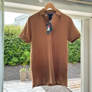 Brun pikétröja Tommy Hilfiger XS - Helt ny!! Snygg brun pikétröja från Tommy Hilfiger i slim fit-modell. Klassisk krage, korta ärmar och liten broderad logga på bröstet. Tillverkad i bomull med pikéstruktur, perfekt för en clean och stilren look.