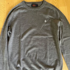 Grå merinoulltröja från Morris - Snygg grå tröja från Morris i 100% merinoull. Klassisk rund halsringning och diskret broderad logga på bröstet. Perfekt för dig som gillar stilrena och bekväma plagg med premiumkänsla. Långärmad och passar till många olika outfits.
