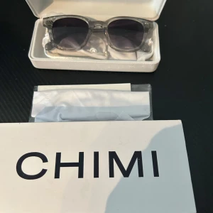 CHIMIS modell 02 solglasögon  - Snygga solglasögon från CHIMI i modell 02 med transparent grå båge och gråtonade glas. Rektangulär form som ger en modern vibe. Kommer med originaletui och putsduk. Perfekta för dig som vill ha en clean och stilren look.