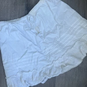 Vit volangkjol från Bon'A Parte Kids - Supersöt vit kortkjol från Bon'A Parte Kids med volangkant och broderade detaljer längst ner. Kjolen har snörning i midjan och är gjord i mjuk bomull. Perfekt för en somrig look med romantiska vibes. Den har fått en ljus ljus ljus gul fläck som knappt syns och kan nog tvättas bort med galltvål eller liknande 💕