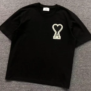 Svart t-shirt från Ami Alexander mattiussi - Svart t-shirt från Ami Paris med stor vit broderad hjärtdetalj och bokstaven A på bröstet. Klassisk rund halsringning och avslappnad passform. Tillverkad i mjuk bomull, perfekt för en clean och stilren look.