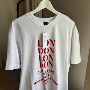 Printed oversized t-shirt - Gina Tricot - Vit oversized t-shirt från Gina Tricot med röd textprint 'LONDON CALLING 1980's' framtill. T-shirten har rund halsringning och korta ärmar. Tillverkad i 100% mjuk bomull för en chill och avslappnad vibe. Helt ny, ny pris: 259,95kr