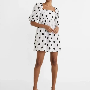 Vit kort klänning med svarta prickar - Superfin vit kort klänning med stora svarta prickar och puffärmar. Klänningen har fyrkantig ringning, öppen rygg med knyt och voluminösa ärmar som ger en trendig look. Tyvärr så kommer det inte till användning då den är lite för kort för mig som är 175cm🥲 Sitter bra på en som bär storlek S men är egentligen storlek M