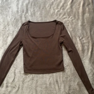 Brun ribbad långärmad topp Shein - Brun långärmad topp från Shein med fyrkantig urringning och croppad passform. Toppen är ribbad och har en tight siluett som sitter snyggt på kroppen. Perfekt att styla med jeans eller kjol för en trendig look.