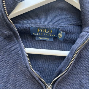Marinblå half zip tröja Polo Ralph Lauren - Snygg marinblå tröja från Polo Ralph Lauren i mjuk pima bomull. Klassisk half zip med hög krage och broderad logga på bröstet. Långärmad modell med ribbade muddar och avslappnad passform. Perfekt för lager-på-lager och stilren vardagslook. Inga skador alls.