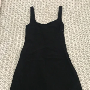 Svart kort klänning från H&M Divided - En svart, enkel och stilren kort klänning från H&M Divided. Klänningen har breda axelband, rundad halsringning med söt spetskant och dragkedja i sidan. Perfekt för dig som gillar minimalistisk och klassisk stil.