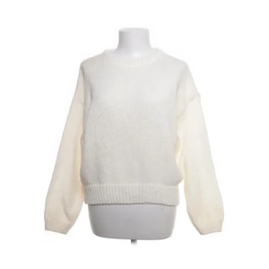 Vit stickad tröja med rund hals - Mysig vit stickad tröja med rund halsringning och breda ribbade muddar vid ärmslut och nederkant. Tröjan har en avslappnad passform och långa ärmar, perfekt för lager-på-lager under kyliga dagar.