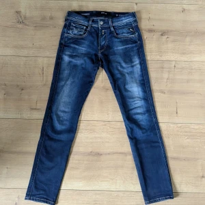 Replay Anbass jeans blå, stl 29 - Snygga Replay Anbass jeans i mörkblå tvätt med diskreta slitningar och klassiska femficksdetaljer. Jeansen har slim passform och raka ben, tillverkade i mjukt denimtyg som sitter skönt hela dagen.